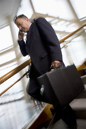 Businessman walking down stairs and talking on cell phone Stock Photo - Premium Royalty-Free, Code: 640-01349368