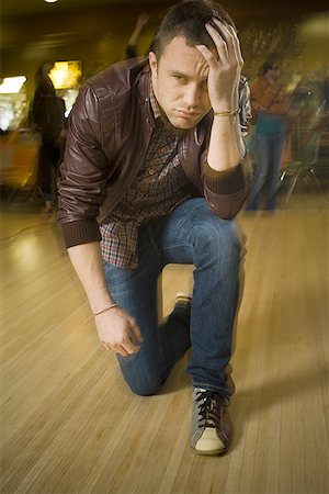 Young man kneeling with his hand on his forehead at a bowling alley Stock Photo - Premium Royalty-Free, Code: 640-01349699