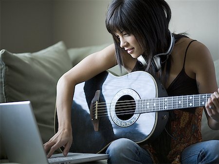 Woman sitting on sofa with laptop and guitar Stock Photo - Premium Royalty-Free, Code: 640-01355152