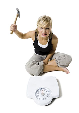 Frustrated dieting woman smashing bathroom scale with a hammer Stock Photo - Premium Royalty-Free, Code: 640-01356314