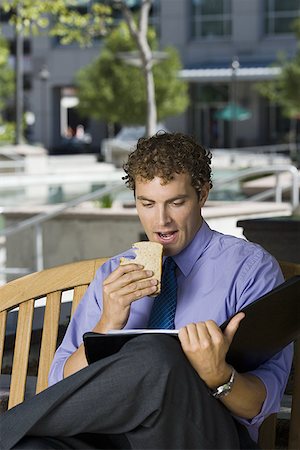 Businessman sitting on a bench, eating a sandwich Stock Photo - Premium Royalty-Free, Code: 640-01356359