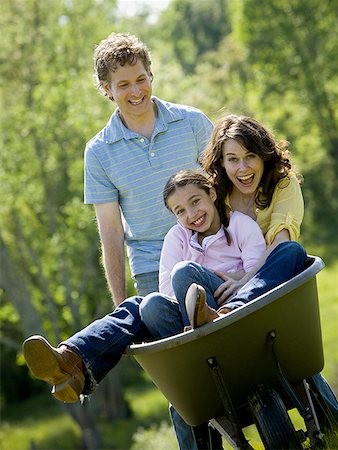 woman and her daughter sitting in a wheel barrow with a man standing beside them Stock Photo - Premium Royalty-Free, Code: 640-01356962