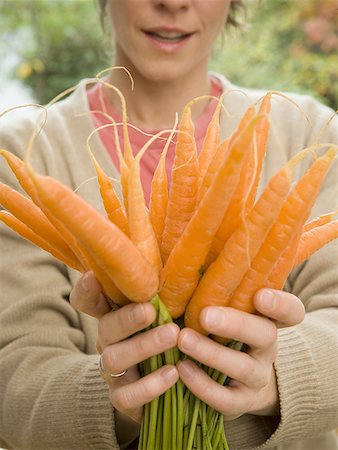 Close-up of an adult woman holding a bunch of carrots Stock Photo - Premium Royalty-Free, Code: 640-01357174