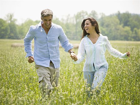 Mature man and a mid adult woman holding hands and running in a field Stock Photo - Premium Royalty-Free, Code: 640-01357319