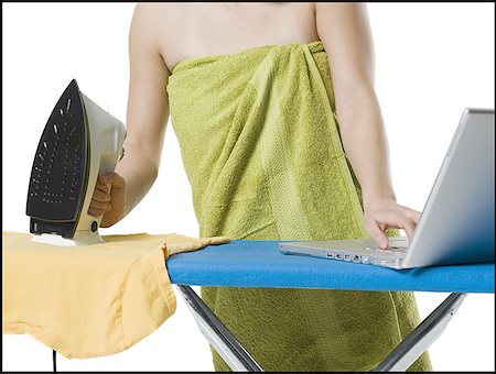 Mid section view of a young woman holding a iron while using a laptop Stock Photo - Premium Royalty-Free, Code: 640-01357726