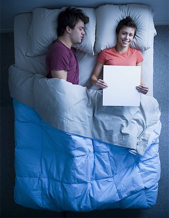 sleeping bed full body - Man asleep in bed and woman holding blank sign smiling Stock Photo - Premium Royalty-Free, Code: 640-01357944