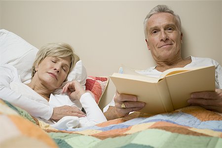 Portrait of a senior man reclining on a bed holding a book while a senior woman sleeps Stock Photo - Premium Royalty-Free, Code: 640-01357969