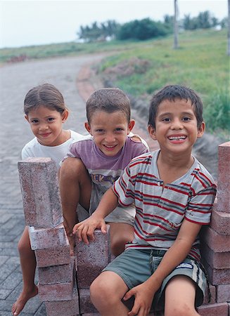 Portrait of two boys and a girl sitting on bricks Stock Photo - Premium Royalty-Free, Code: 640-01358076