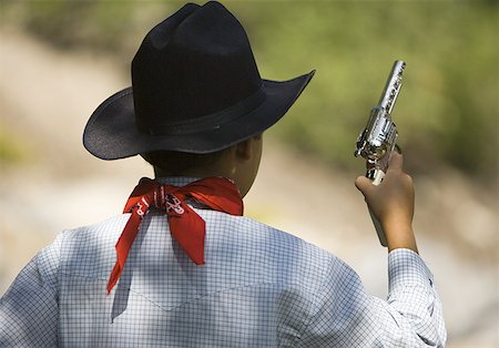 Rear view of a boy in a cowboy costume holding a toy gun Stock Photo - Premium Royalty-Free, Code: 640-01358592