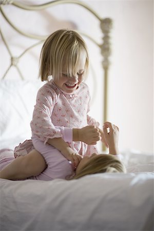 Girl sitting on top of her sister in a bedroom, smiling Fotografie stock - Premium Royalty-Free, Codice: 640-01359012