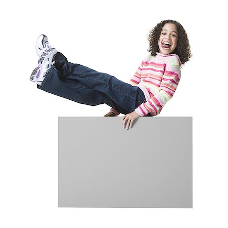 Portrait of a girl sticking her tongue out and sitting on a blank sign Stock Photo - Premium Royalty-Free, Code: 640-01359409