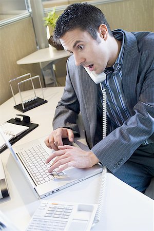 High angle view of a businessman using a laptop and talking on the telephone Stock Photo - Premium Royalty-Free, Code: 640-01359670