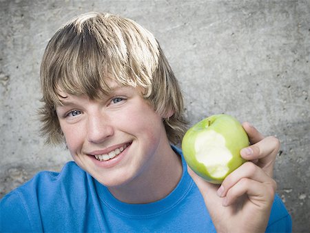 Portrait of a teenage boy holding an apple and looking cheerful Stock Photo - Premium Royalty-Free, Code: 640-01359913
