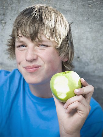 Portrait of a teenage boy eating an apple and smiling Stock Photo - Premium Royalty-Free, Code: 640-01350503