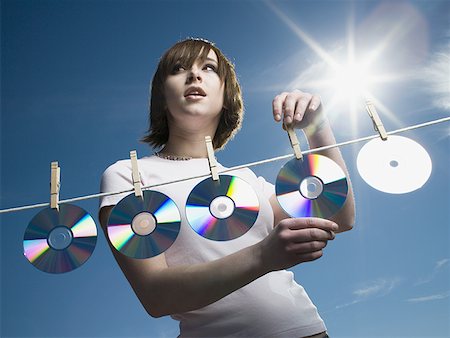 Low angle view of a teenage girl drying CDs on a clothesline Stock Photo - Premium Royalty-Free, Code: 640-01350665