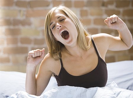 Close-up of a young woman sitting on a bed yawning Fotografie stock - Premium Royalty-Free, Codice: 640-01351011