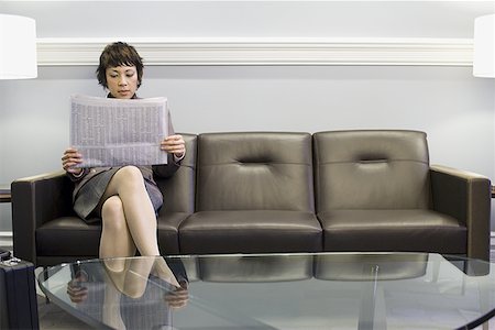 Businesswoman sitting on a couch and reading a newspaper Stock Photo - Premium Royalty-Free, Code: 640-01351432