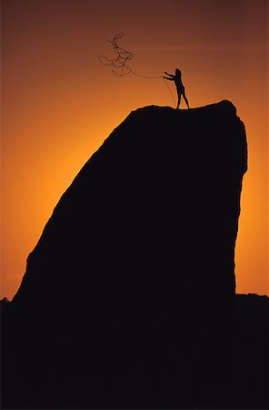 Silhouette of a person standing on the top of a rock throwing out a rope Stock Photo - Premium Royalty-Free, Code: 640-01351472