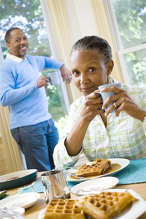 Portrait of a senior woman sitting at the breakfast table with a senior man standing behind her Stock Photo - Premium Royalty-Free, Code: 640-01352237