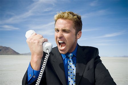 Close-up of a businessman shouting in front of a telephone receiver Stock Photo - Premium Royalty-Free, Code: 640-01352720