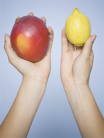 Close-up of human hands holding a lemon and a mango Stock Photo - Premium Royalty-Free, Code: 640-01353021