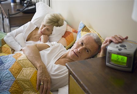 Homme senior au lit atteignant l'alarme alors que sa femme dort Photographie de stock - Premium Libres de Droits, Code: 640-01353608