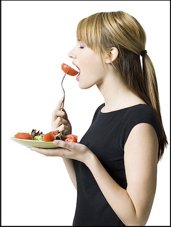 Profile of a young woman eating a slice of tomato Stock Photo - Premium Royalty-Free, Code: 640-01353902