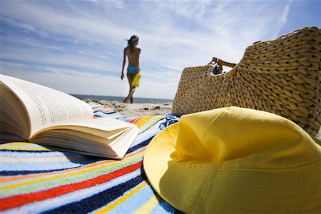 Beach towel with book and bag with a young woman in background Stock Photo - Premium Royalty-Free, Code: 640-01364460