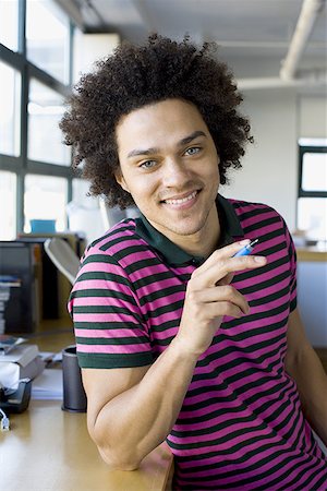 Portrait of a young man holding a pen and smiling Stock Photo - Premium Royalty-Free, Code: 640-01364847