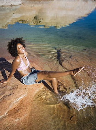 High angle view of a young woman sitting on a rock, splashing water Stock Photo - Premium Royalty-Free, Code: 640-01366163
