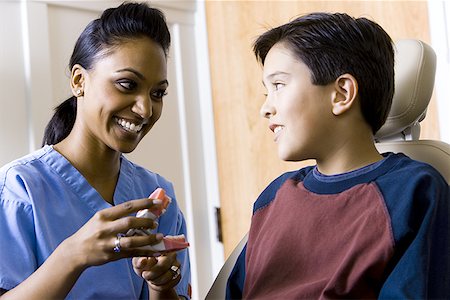 dentist patient talking - Dental hygienist holding false teeth talking to boy Stock Photo - Premium Royalty-Free, Code: 640-01360355