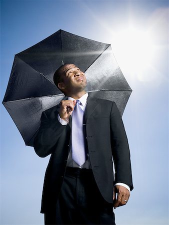 sun sky rain - Businessman holding umbrella on a clear day Stock Photo - Premium Royalty-Free, Code: 640-01360916