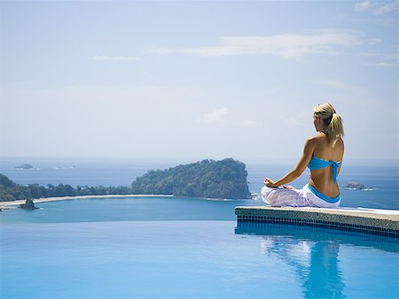 Rear view of a mid adult woman sitting in a lotus position at the poolside and meditating Stock Photo - Premium Royalty-Free, Code: 640-01361895