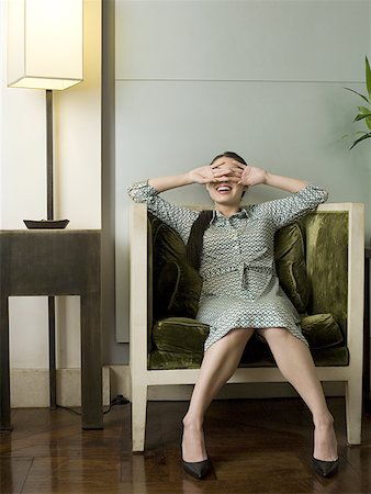 Young woman sitting in an armchair covering her eyes Stock Photo - Premium Royalty-Free, Code: 640-01362715