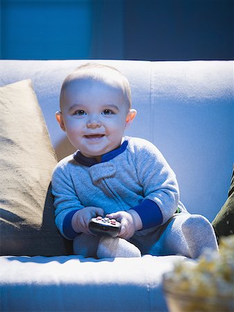 Baby on sofa with television remote smiling Stock Photo - Premium Royalty-Free, Code: 640-01458588