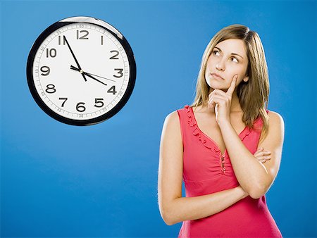 Woman with arms crossed looking at wall clock attached to plumbing pipes Stock Photo - Premium Royalty-Free, Code: 640-01458897