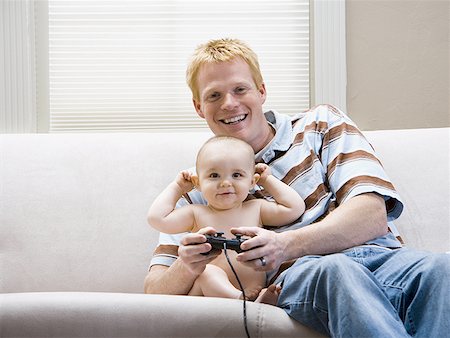 simsearch:640-01458949,k - Homme et bébé sur le canapé avec le contrôleur de jeu vidéo sourire Photographie de stock - Premium Libres de Droits, Code: 640-01458924