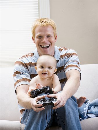 simsearch:640-01458949,k - Homme et bébé sur le canapé avec le contrôleur de jeu vidéo sourire Photographie de stock - Premium Libres de Droits, Code: 640-01458922