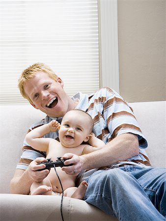 simsearch:640-01458949,k - Homme et bébé sur le canapé avec le contrôleur de jeu vidéo sourire Photographie de stock - Premium Libres de Droits, Code: 640-01458923