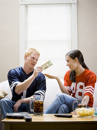 football fan on couch - Man giving woman money both in football jerseys Stock Photo - Premium Royalty-Free, Code: 640-01458931