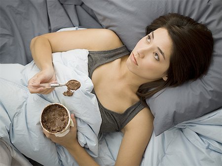 depression and chocolate - Woman lying down in bed spilling chocolate ice cream on blanket Stock Photo - Premium Royalty-Free, Code: 640-01574819