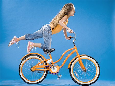 en avant - Fille sur vélo orange à genoux sur le siège avec le pied vers le haut Photographie de stock - Premium Libres de Droits, Code: 640-01574949
