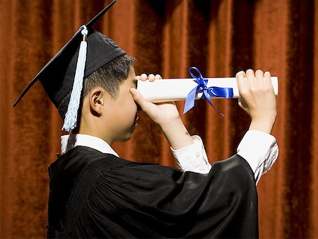 Profile of boy graduate with mortar board looking through diploma Stock Photo - Premium Royalty-Free, Code: 640-01574978