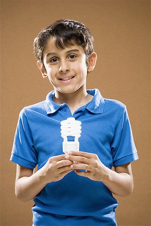 Boy holding energy efficient lightbulb smiling Stock Photo - Premium Royalty-Free, Code: 640-01575101