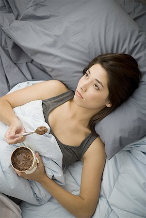 sadness and icecream - Woman lying in bed eating chocolate ice cream Stock Photo - Premium Royalty-Free, Code: 640-01575208