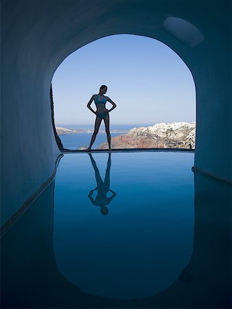 Silhouette of woman in bikini standing at edge of infinity pool with arch and rock formation Stock Photo - Premium Royalty-Free, Code: 640-01575363