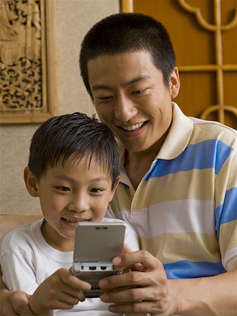 sofa two boys video game - Father and son looking at portable electronic device Stock Photo - Premium Royalty-Free, Code: 640-01601426