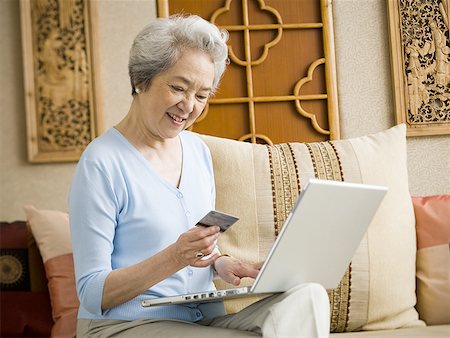 simsearch:640-02775245,k - Woman sitting on sofa with laptop and credit card smiling Stock Photo - Premium Royalty-Free, Code: 640-01601462