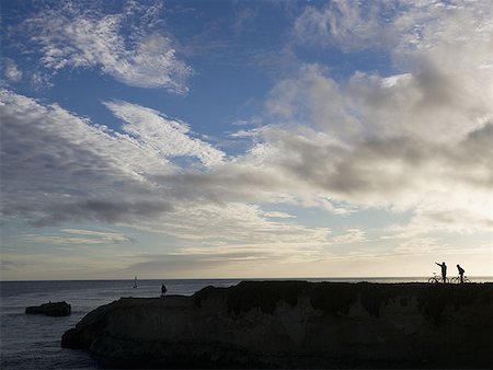 simsearch:640-03259527,k - Silhouette of people with bicycles on rock at water with blue sky and clouds Stock Photo - Premium Royalty-Free, Code: 640-01601788