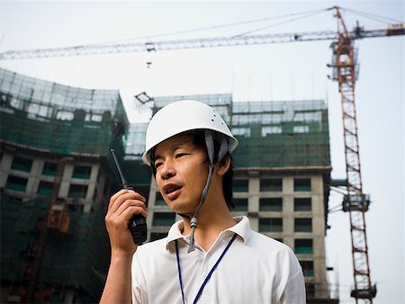 simsearch:640-03265269,k - Man with construction helmet and crane in background holding walkie talkie Foto de stock - Sin royalties Premium, Código: 640-01645365